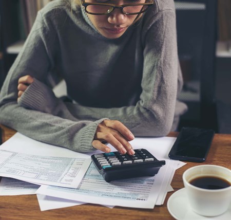 A person calculating their debt with a calculator and bills