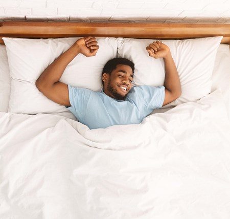 Person happy and lying in bed after a good sleep. Using tips to improve sleep. Longer, restful and deeper sleep.